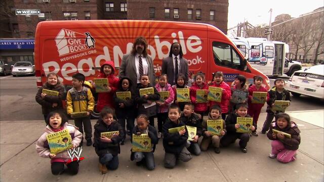 Kofi Kingston & Mick Foley participate in a reading celebration background