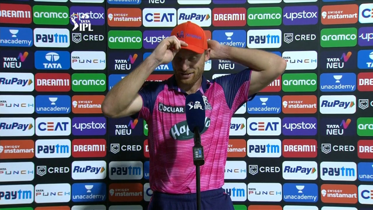M13: RR vs RCB – Aramco Orange Cap Holder – Jos Buttler background